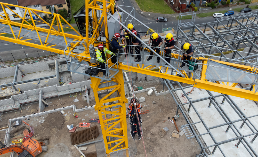 Fire crew on in full safety gear on top of large yellow crane, high above a construction site. 