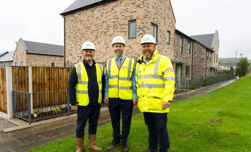 Three people standing on grass in front of new-build brick homes, in high visibility construction clothes.